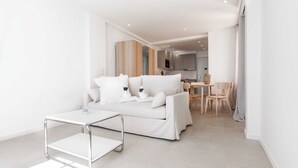 A modern, minimalist living room with a white sofa, a glass coffee table, and a dining area with wooden chairs and a small table. - Charming Studio - 2p/ac - Sea View - Antibes (Antibes)