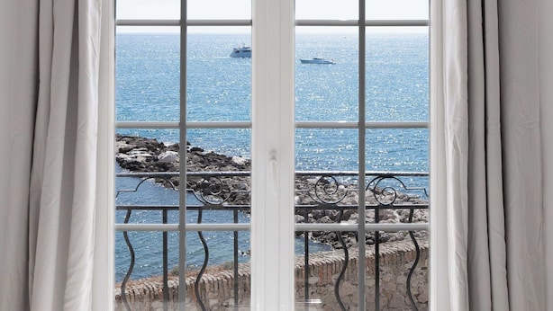 A room with a large window featuring a view of the sea and rocky coastline. - Charming Studio - 2p/ac - Sea View - Antibes (Antibes)