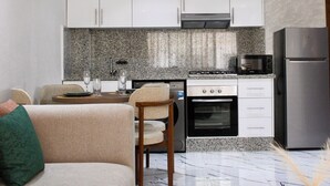 A modern kitchen with white cabinets, a granite countertop, a built-in oven, a microwave, and a stainless steel refrigerator.
