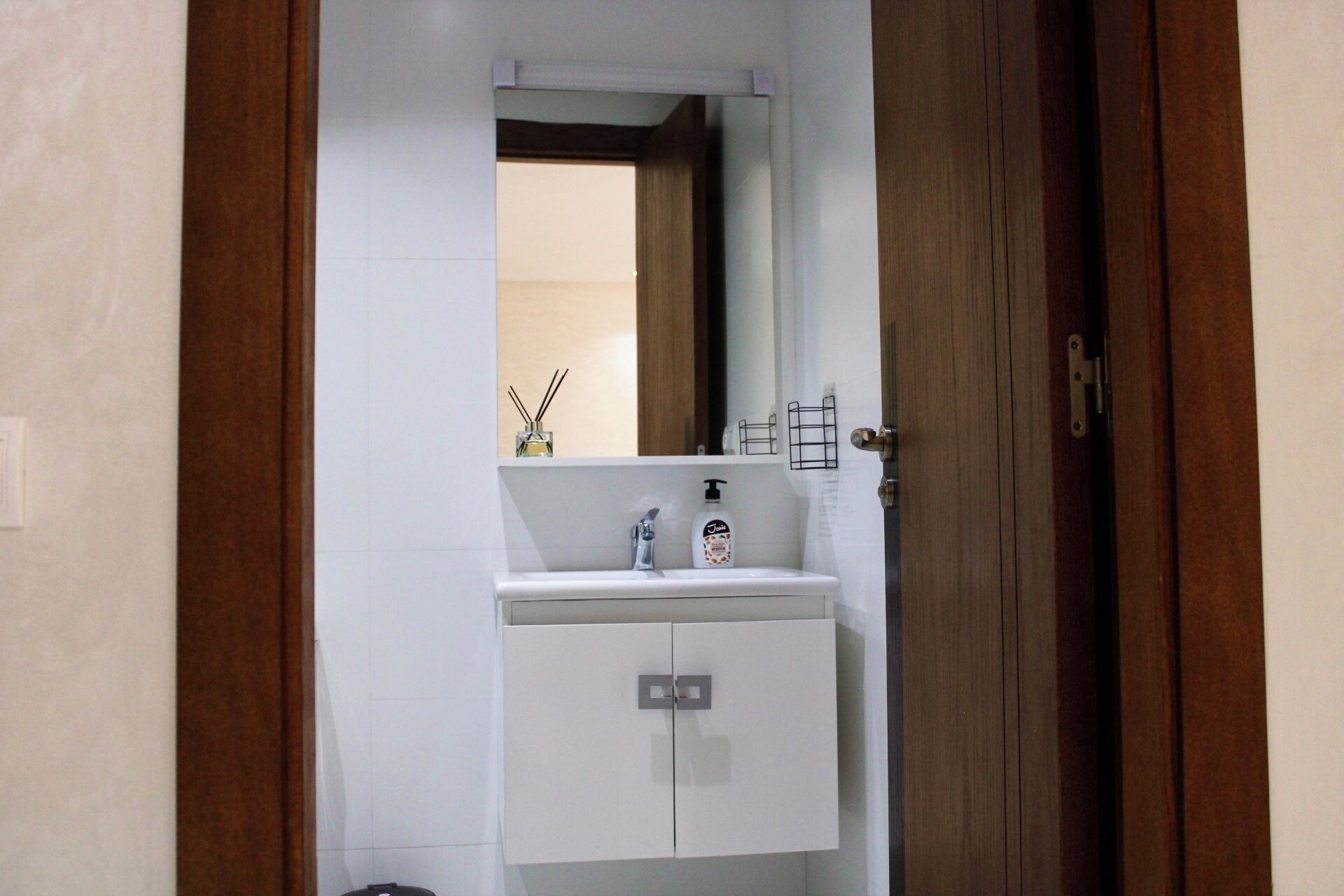Une salle de bain avec un lavabo blanc, un miroir au-dessus et une porte en bois.