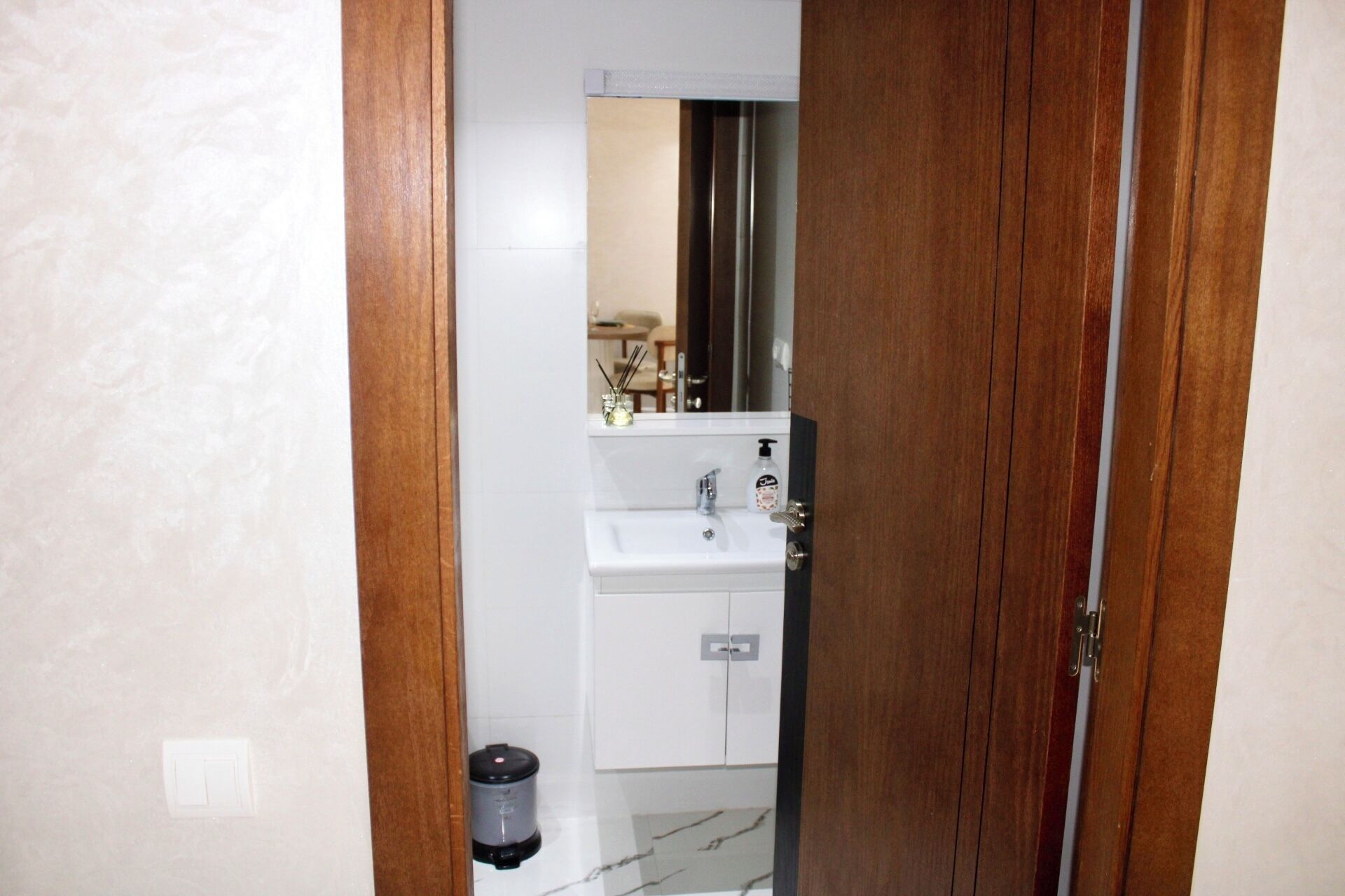 Une salle de bain avec un lavabo blanc, un miroir et une poubelle.