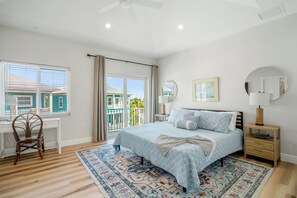 Un dormitorio con cama, escritorio, silla, ventana y balcón.