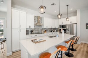 Una cocina moderna con gabinetes blancos, una isla grande, electrodomésticos de acero inoxidable e iluminación colgante.