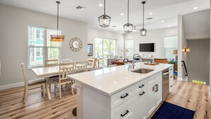 Une cuisine moderne dotée d’un îlot central, de luminaires suspendus et d’un coin repas avec des chaises en bois.