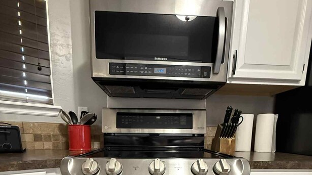 Una cocina con armarios blancos, estufa de acero inoxidable, microondas y tostadora.
