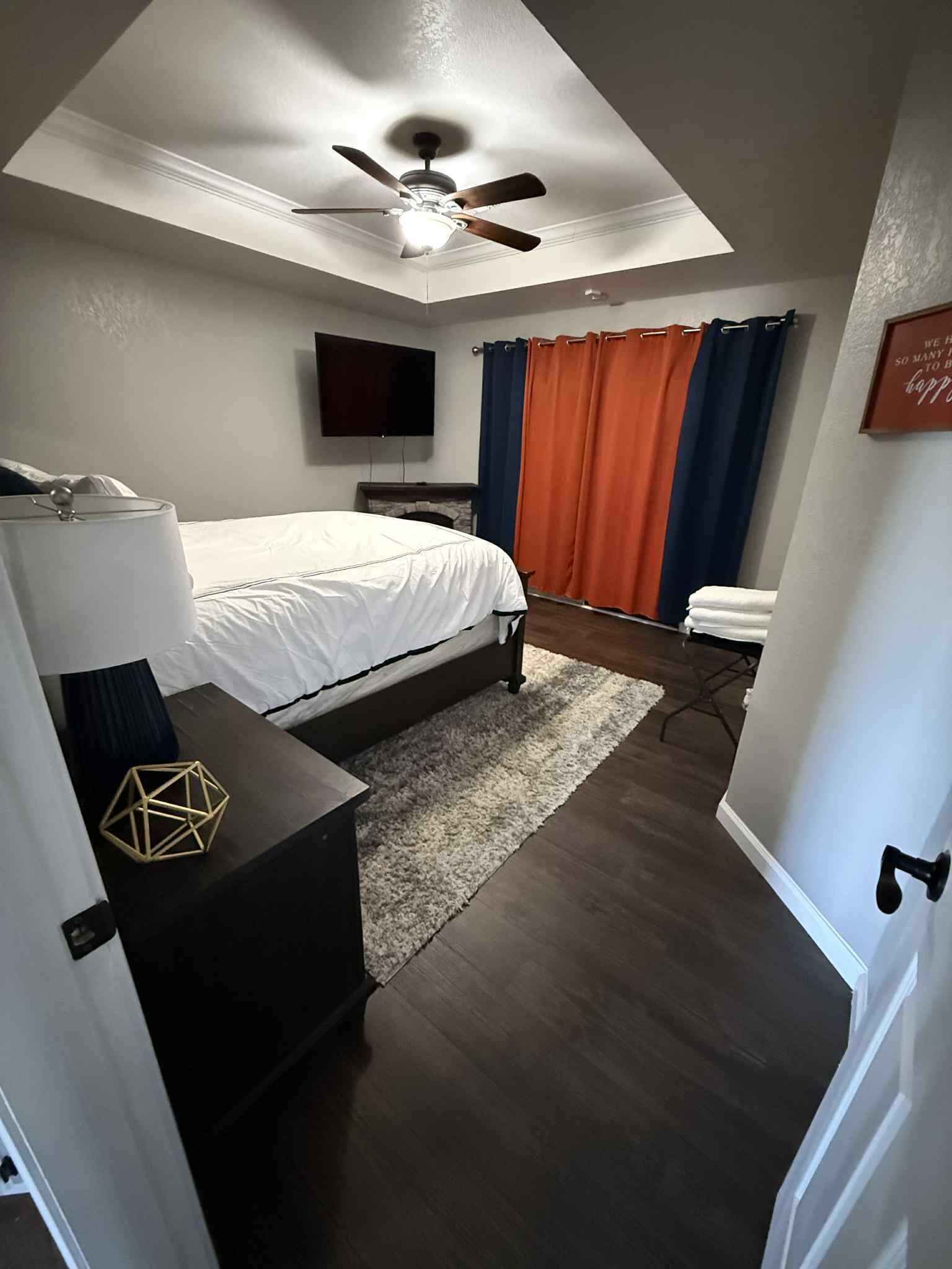 A bedroom with a bed, a ceiling fan, a TV, and a fireplace.