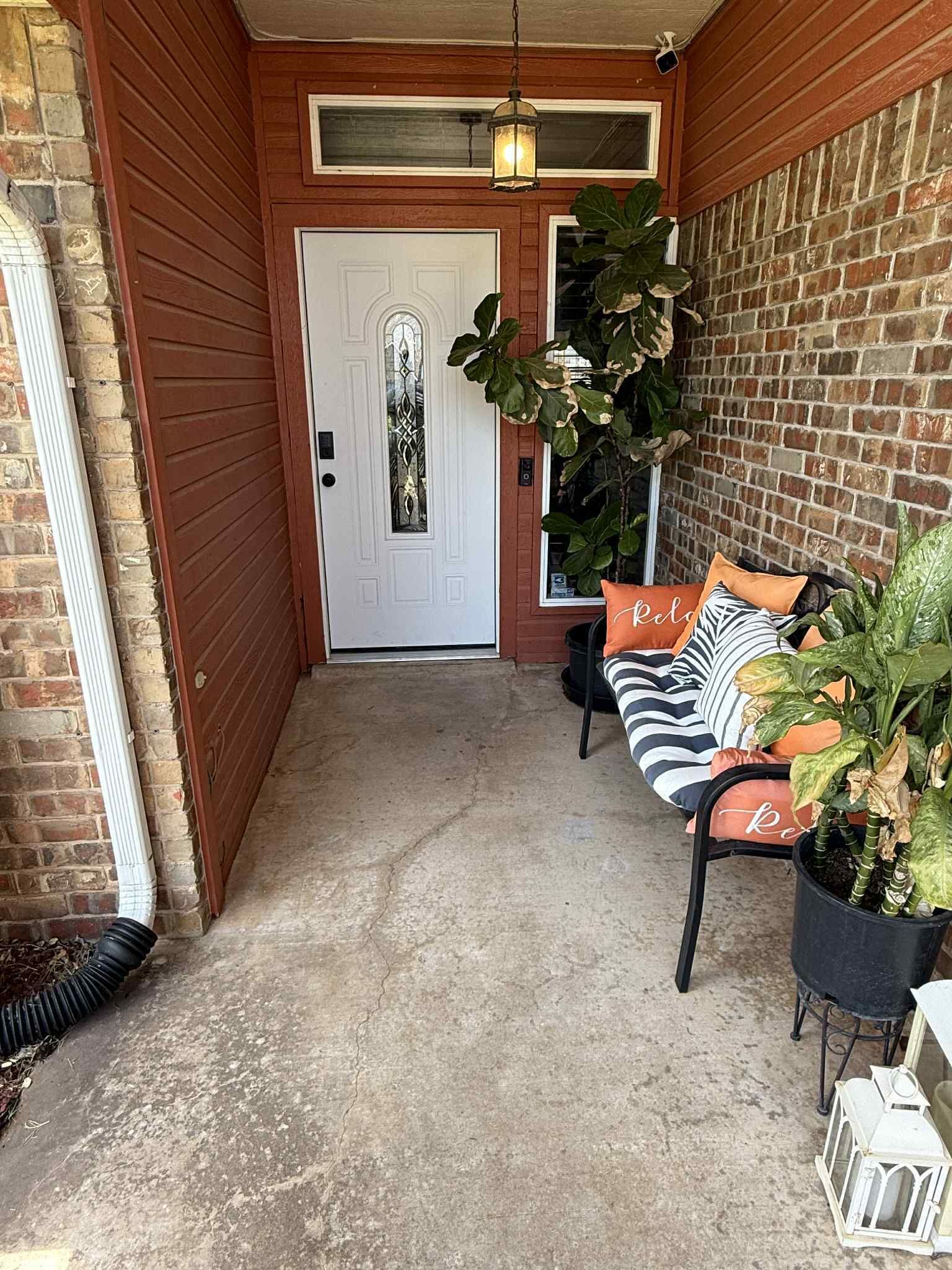 A covered porch with a bench, potted plants, and a door.