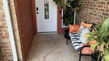 A covered porch with a bench, potted plants, and a door.