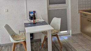 A small dining area with a table, chairs, a bottle of wine, and a glass. A TV is mounted on the wall above the table.