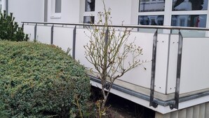 A white building with a balcony, a small window, and a hedge.