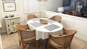 Comedor con una mesa redonda, seis sillas de mimbre, una lámpara de araña, obras de arte enmarcadas en la pared y una ventana con persianas.