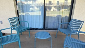 Un patio con cuatro sillas azules y una pequeña mesa, una puerta corrediza de vidrio y vistas a un edificio con mesas al aire libre.