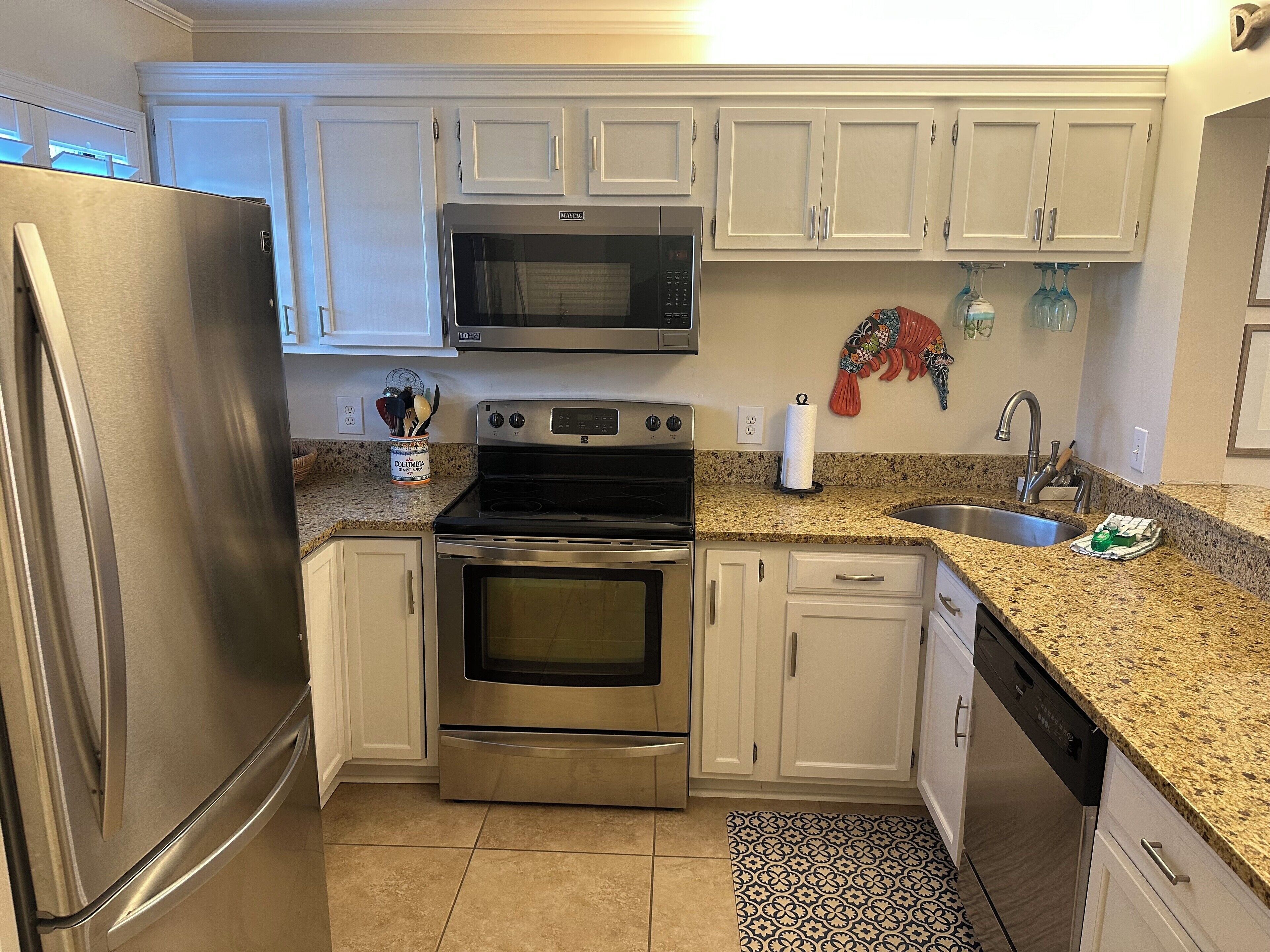 A kitchen with white cabinets, stainless steel appliances, a granite countertop, and a patterned rug.