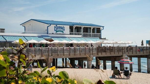 A beachside restaurant with outdoor seating and a pier extending over the water.