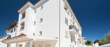 A white multi-story building with balconies and a covered outdoor seating area.