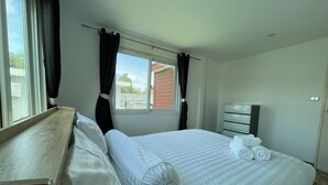 A neatly made bed with white linens and a pillow, a wooden headboard, a window with curtains, and a small bedside table. - Quiet 2 bedroom house in Rawai (Rawai)