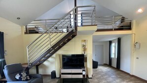 A spacious living room with a high ceiling, a staircase leading to an upper level, a flat-screen TV, a coffee table, and a sofa. - Quiet 2 bedroom house in Rawai (Rawai)