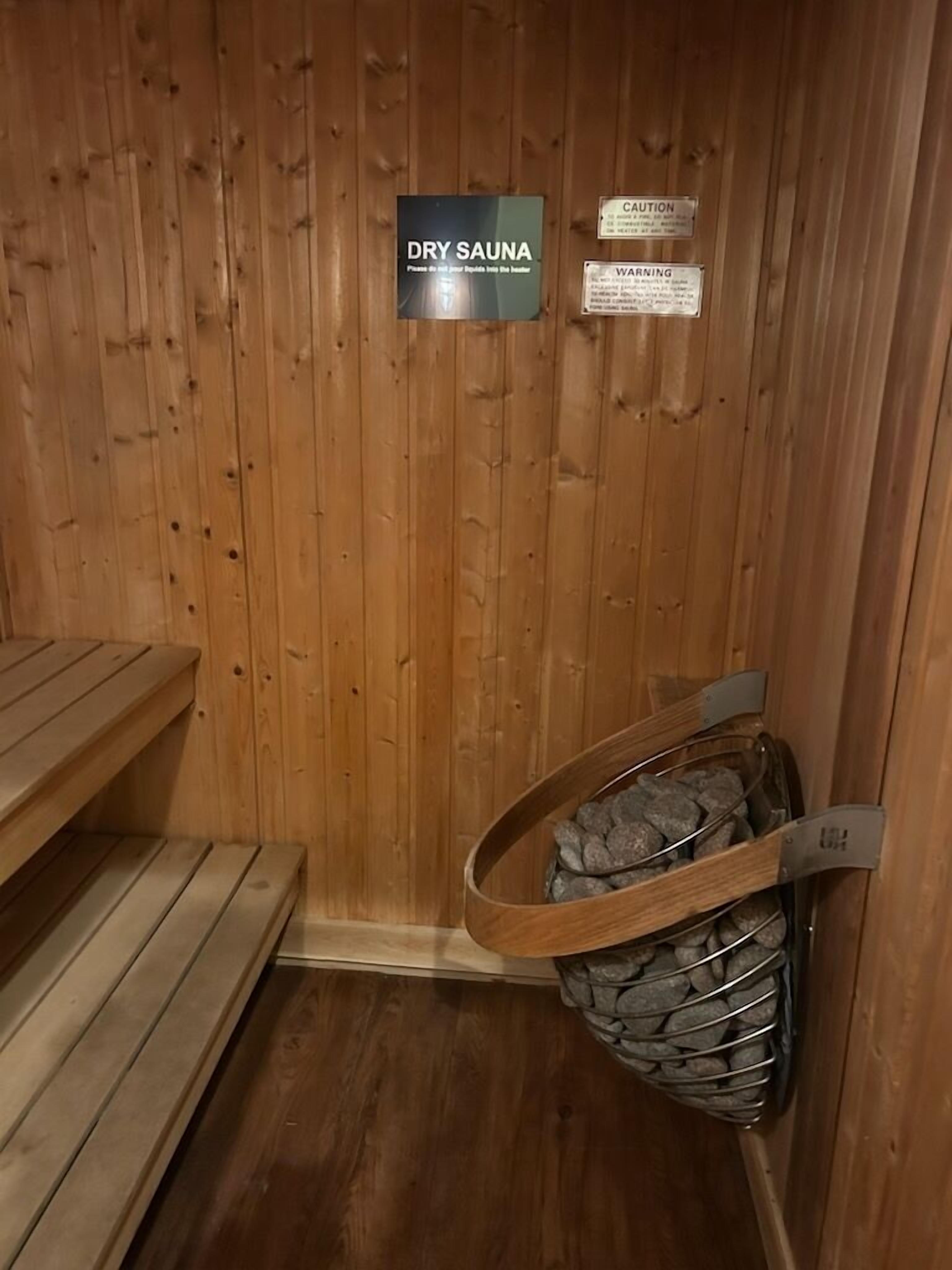 Uma sauna seca com paredes de madeira, um banco e uma cesta de metal cheia de pedras.