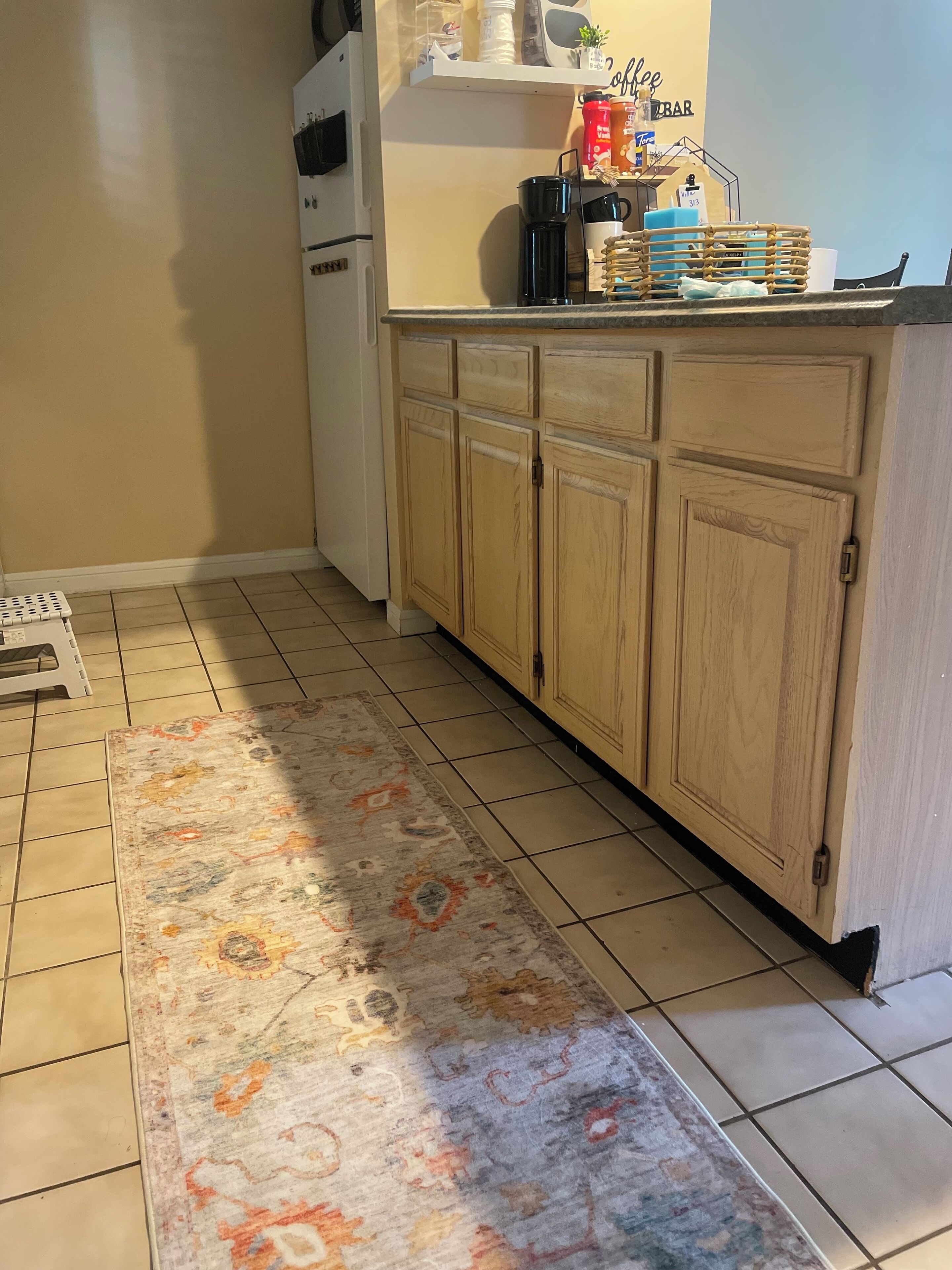 A kitchen with wooden cabinets, a coffee bar, and a patterned rug.