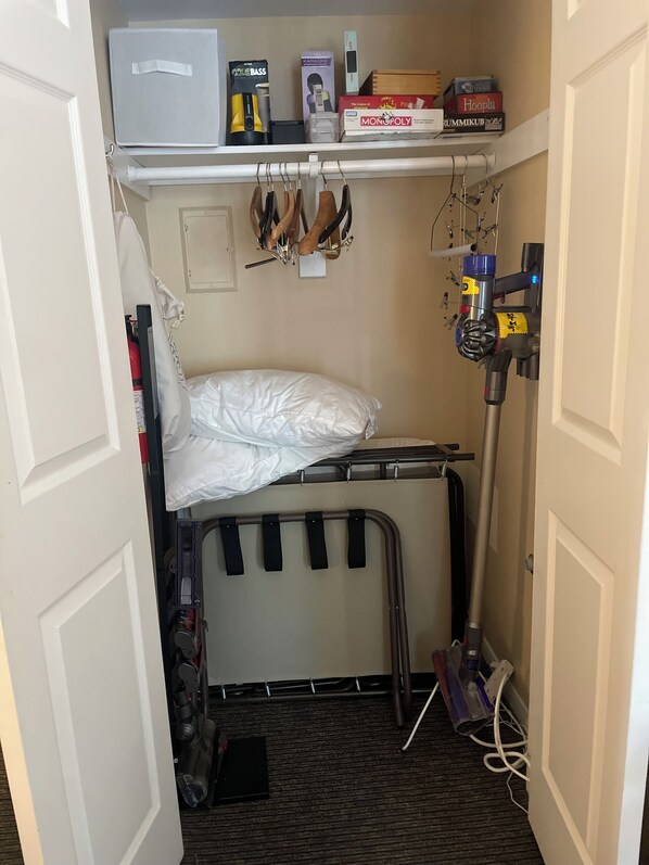 Een kleine, compacte kamer met een stapelbed, een plank vol spelletjes en een stofzuiger.