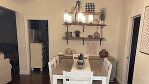 Een eetruimte met een houten tafel en witte stoelen, een kroonluchter en planken met decoratieve objecten.