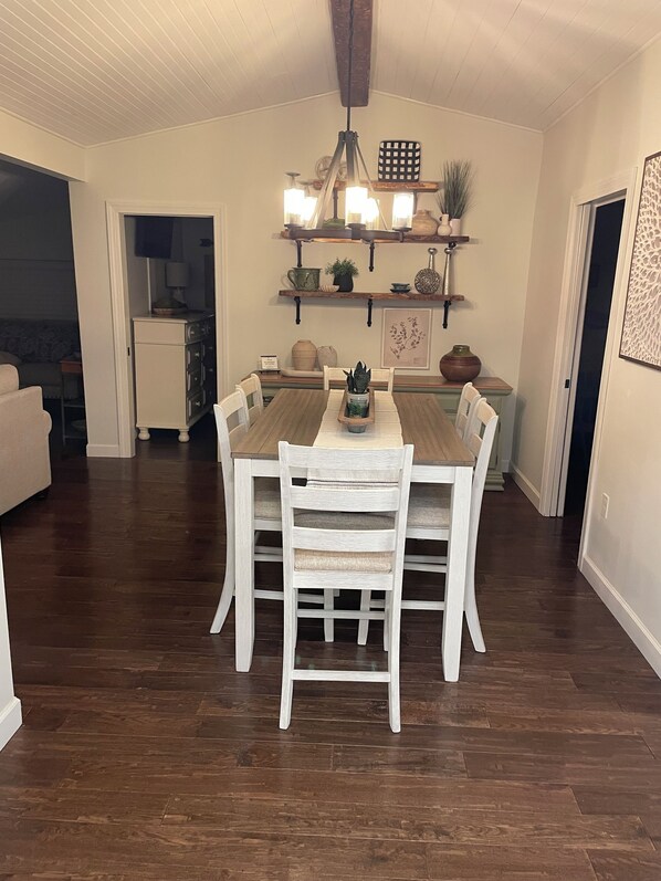 A dining area with a wooden table and white chairs, a chandelier, and shelves with decorative items. - Charming 3-bedroom Lakehouse . Boat Slip, Pontoon option .3 Golf courses nearby (Rutledge)