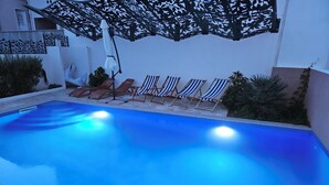 A swimming pool with blue water, surrounded by lounge chairs and a decorative canopy.