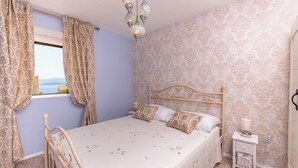 A bedroom with a bed, curtains, a nightstand, and a chandelier.