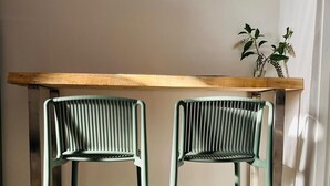 Deux chaises en métal avec un dossier en osier, une table en bois et une plante en pot, le tout posé sur un sol carrelé.