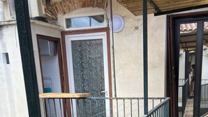 Un balcon avec une balustrade en métal, une porte dotée d’un panneau en verre dépoli et un sol carrelé.