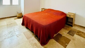 Une chambre à coucher comprenant un lit, une fenêtre, une table de chevet et un luminaire fixé au mur.