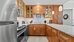 A modern kitchen with wooden cabinets, stainless steel appliances, and a marble countertop. - Ocean Club 1106 | Enjoy Views of the Gulf! (Biloxi)