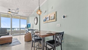 A modern living room with a dining area, large windows, and a view of the ocean. - Ocean Club 1106 | Enjoy Views of the Gulf! (Biloxi)