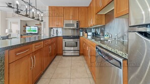 A modern kitchen with wooden cabinets, stainless steel appliances, and a granite countertop. - Ocean Club 204 Deluxe | Stunning Panoramic Views of the Gulf! (Biloxi)
