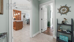 A hallway with a wooden cabinet, pendant lights, a ship's wheel, and a shelf with decorative items. - Ocean Club 204 Deluxe | Stunning Panoramic Views of the Gulf! (Biloxi)