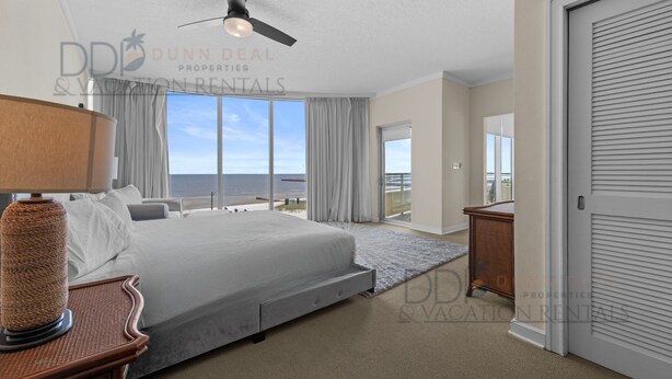 A spacious bedroom with a large bed, a ceiling fan, and a view of the ocean. - Ocean Club 204 Deluxe | Stunning Panoramic Views of the Gulf! (Biloxi)