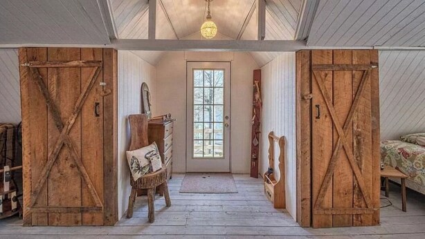 Un intérieur rustique avec des portes de grange en bois, un banc en bois, une commode et un lustre.