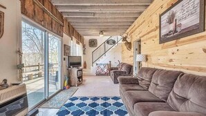Un salon chaleureux avec un grand canapé, un téléviseur et un mur en bois orné d’une tête de cerf.