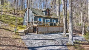 Un chalet avec des fondations en pierre, une terrasse en bois et une grande fenêtre donnant sur une zone boisée.