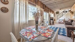 Un salon chaleureux avec un plafond en bois, une table à manger agrémentée d’un chemin de table coloré et un escalier menant à un autre niveau.