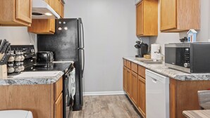 A compact kitchen with wooden cabinets, a black refrigerator, a stove, a microwave, and a dishwasher. - Spacious2BR/Work Crews & Families/Sleeps6/desk/Parking/WIFI/Pet friendly (Aurora)