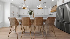 Una cocina moderna con armarios blancos, electrodomésticos de acero inoxidable y una isla central con taburetes de bar.