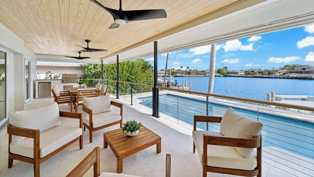 Un balcón amplio con mobiliario de madera, piscina y vista al agua.
