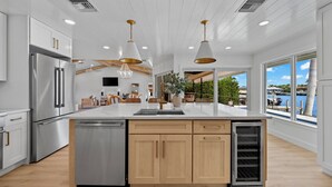 Una cocina moderna con una isla grande, electrodomésticos de acero inoxidable, armarios de madera, iluminación colgante y vistas al agua.