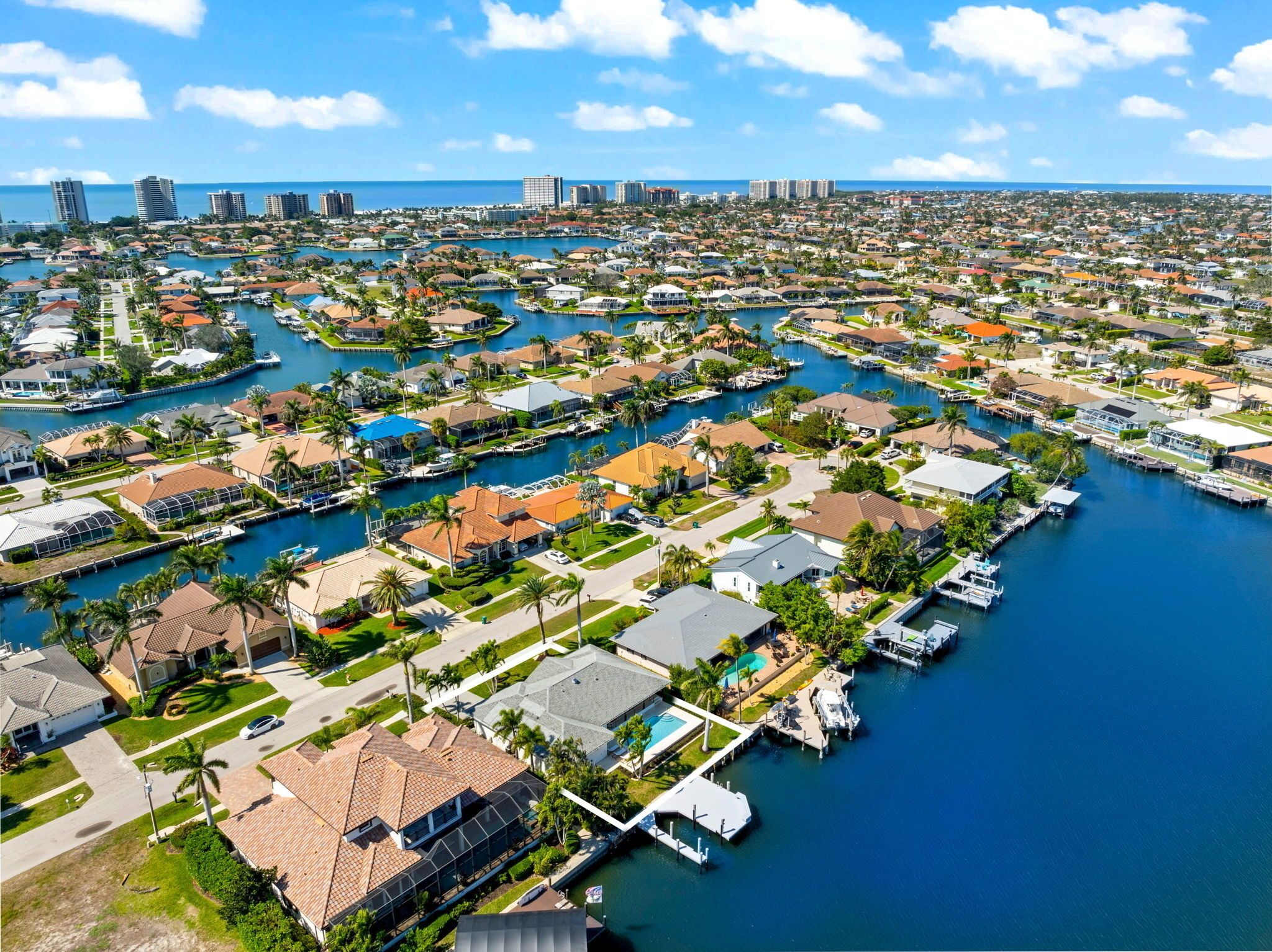 An aerial view of a coastal residential area with numerous houses, docks, and a marina.