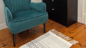 A teal armchair, a black cabinet, and a patterned rug in a room with wooden flooring. - Luxury Capitol 122m² Air-conditioned - Parking & Elevator & Subway (Toulouse)