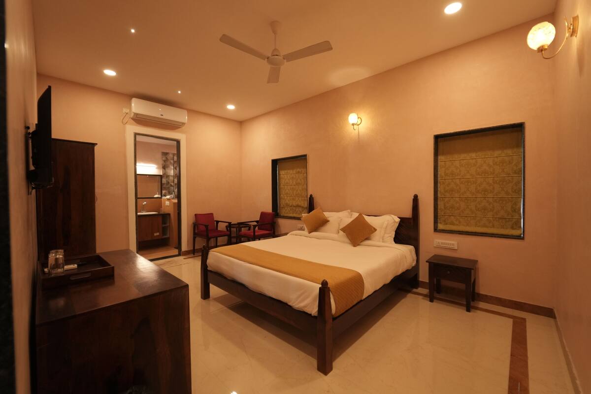 A hotel room with a bed, bedside tables, a desk, a chair, a ceiling fan, and a wall-mounted TV.