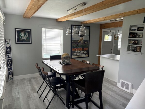 A dining area with a wooden table and chairs, a window with blinds, and a poster on the wall. - RARE CHANCE TO RENT THIS ND HOME 1.45 MILES FROM ND CAMPUS WITH IRISH PUB & MORE (South Bend)
