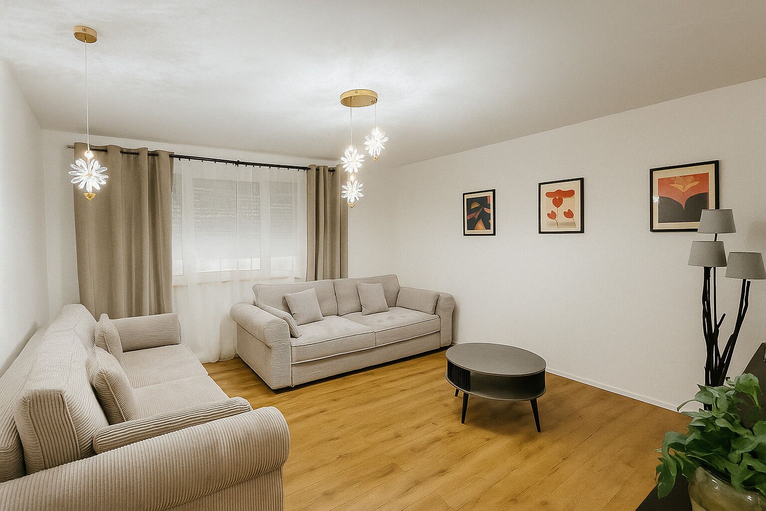 Un salon moderne avec un canapé beige, une table basse ronde et une grande fenêtre avec des rideaux. Trois œuvres d’art encadrées ornent le mur, et une lampe sur pied est placée dans un coin.