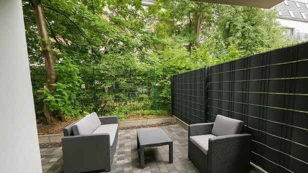 Une terrasse dotée de meubles en osier, d’un sol carrelé et d’un mur noir.